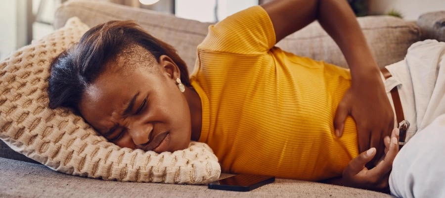 mulher jovem deitada de lado no sofá com dor abdominal