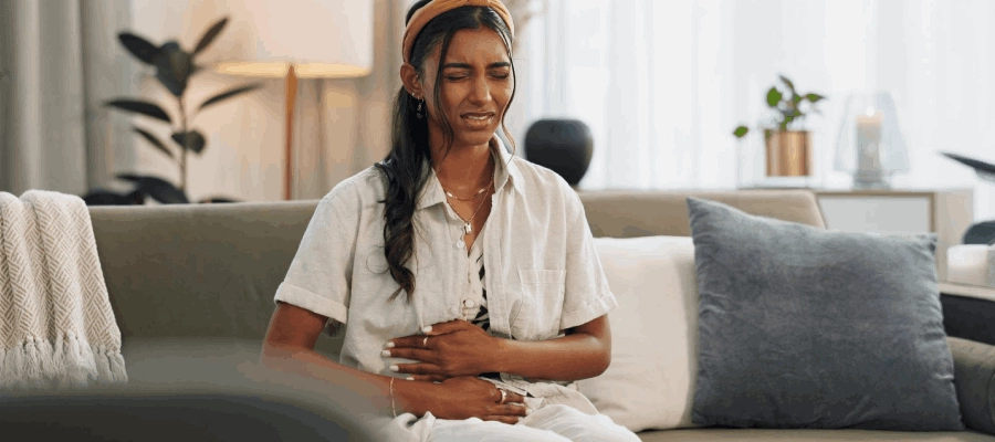 mulher negra sentada no sofá com dor no estômago