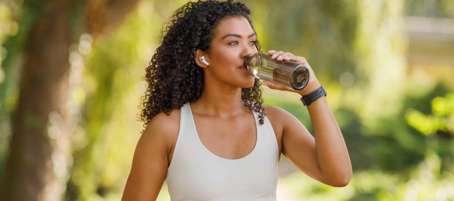 mulher-jovem-bebe-agua-no-parque-ensolarado-ao-ar-livre