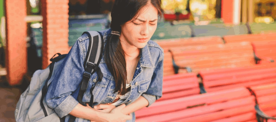 jovem sente azia na escola com a mão na barriga