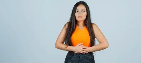 Mulher com expressão de desconforto segurando o abdômen, indicando dor ou mal-estar na barriga.