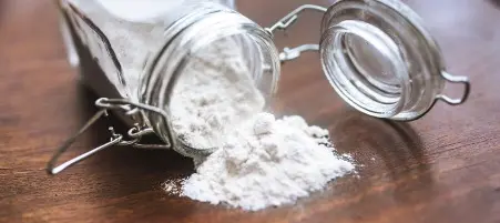 Pote de vidro tombado com bicarbonato de sódio derramado sobre uma superfície de madeira.