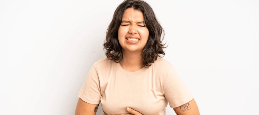 mulher jovem com as mãos na barriga e expressão de dor