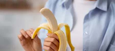 Pessoa segurando e descascando uma banana madura, pronta para o consumo.